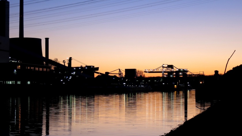Blick in Richtung der gerade untergegangenen Sonne über das Hafenbecken auf Verladebrücken und Industriegebäude. Die Silhouette spiegelt sich im Wasser.