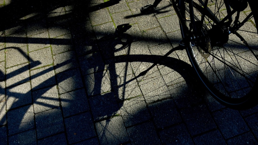 Fahrrad, das auf gepflasterter Fläche abgestellt ist und ein Schattenbild auf diese Fläche wirft